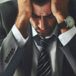 Zoomed in image of businessman with hands on his head and elbows on the table.